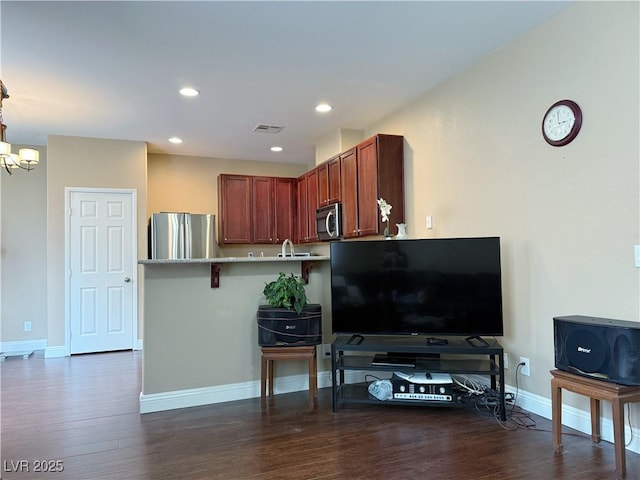 kitchen with baseboards, dark wood-style floors, a peninsula, stainless steel appliances, and a kitchen bar