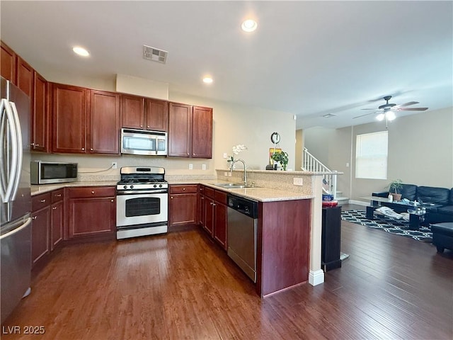 kitchen with dark wood-style floors, stainless steel appliances, open floor plan, a sink, and a peninsula