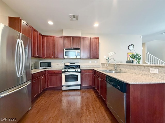 kitchen featuring stainless steel appliances, a peninsula, a sink, visible vents, and dark wood finished floors