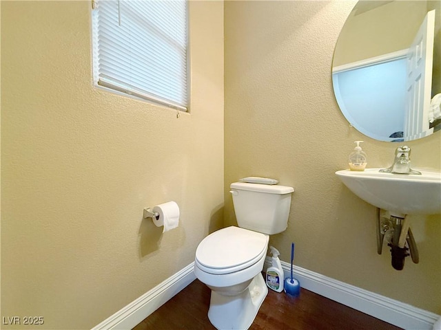 half bathroom with toilet, baseboards, and wood finished floors