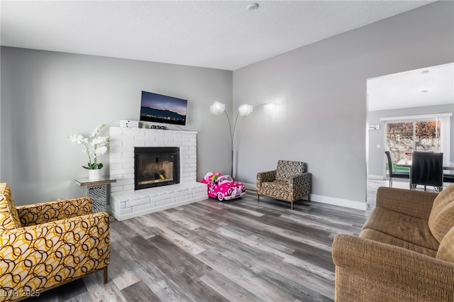 living room featuring vaulted ceiling, a brick fireplace, wood finished floors, and baseboards