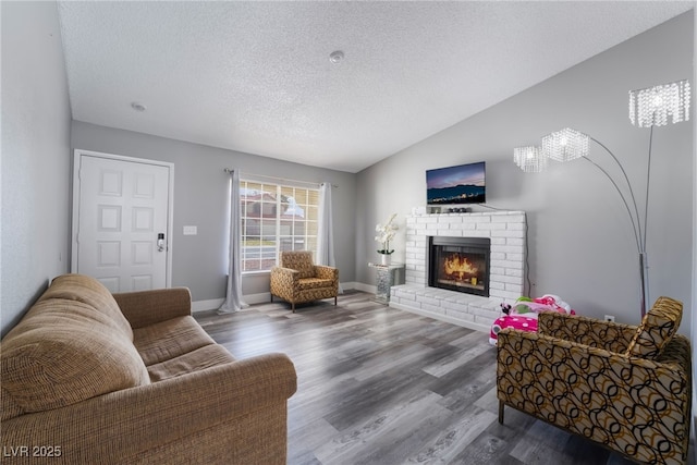 living room featuring lofted ceiling, a brick fireplace, a textured ceiling, wood finished floors, and baseboards