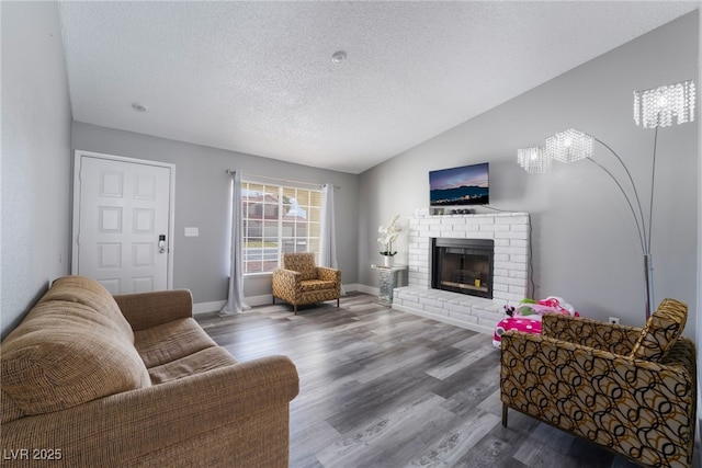 living area featuring a fireplace, vaulted ceiling, a textured ceiling, wood finished floors, and baseboards