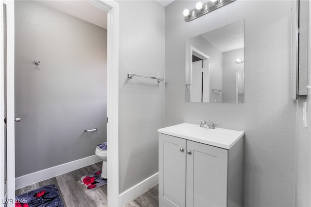 bathroom with toilet, wood finished floors, vanity, and baseboards