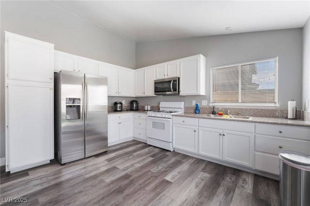 kitchen featuring white cabinets, lofted ceiling, appliances with stainless steel finishes, wood finished floors, and a sink