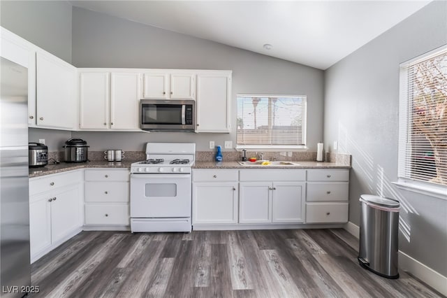 kitchen featuring dark wood-type flooring, vaulted ceiling, stainless steel appliances, white cabinetry, and a sink