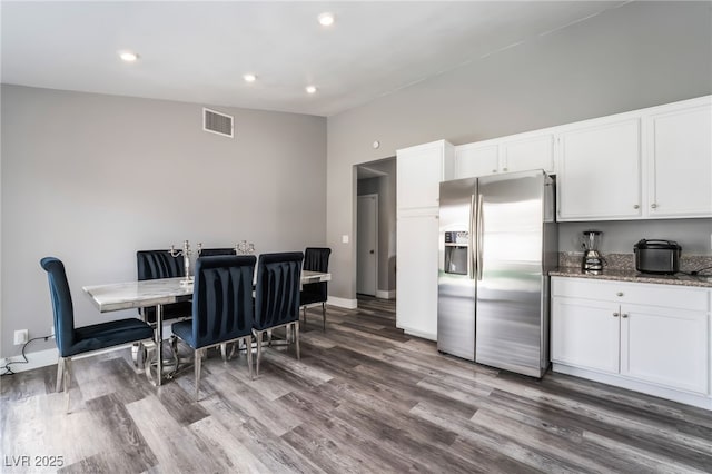 kitchen featuring visible vents, stainless steel fridge with ice dispenser, lofted ceiling, wood finished floors, and white cabinetry