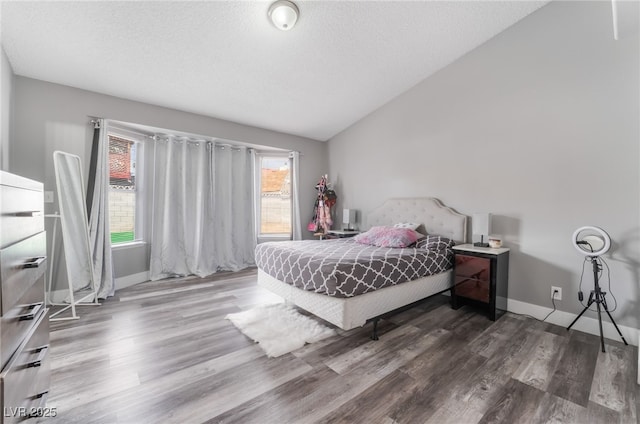 bedroom featuring vaulted ceiling, a textured ceiling, baseboards, and wood finished floors