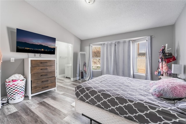 bedroom featuring lofted ceiling, a textured ceiling, baseboards, and wood finished floors