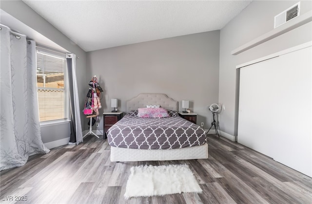 bedroom featuring baseboards, visible vents, wood finished floors, vaulted ceiling, and a textured ceiling