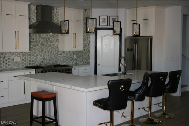 kitchen with wall chimney range hood, backsplash, high quality fridge, and white cabinetry