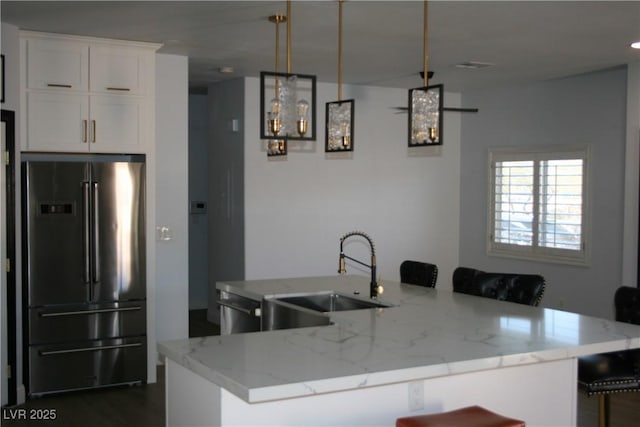 kitchen with a sink, a kitchen breakfast bar, white cabinets, freestanding refrigerator, and light stone countertops