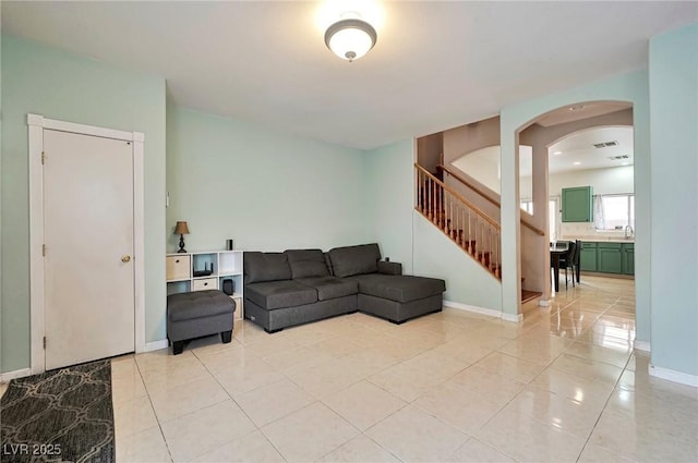 living room with light tile patterned floors, visible vents, baseboards, arched walkways, and stairs