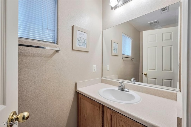 bathroom with a textured wall, visible vents, and vanity