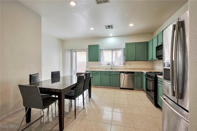 kitchen with light tile patterned floors, green cabinetry, light countertops, black appliances, and a sink