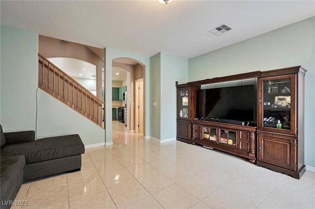 living area with light tile patterned floors, baseboards, visible vents, arched walkways, and stairway