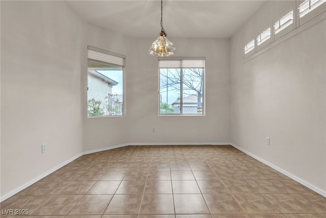 empty room featuring an inviting chandelier, light tile patterned floors, and baseboards