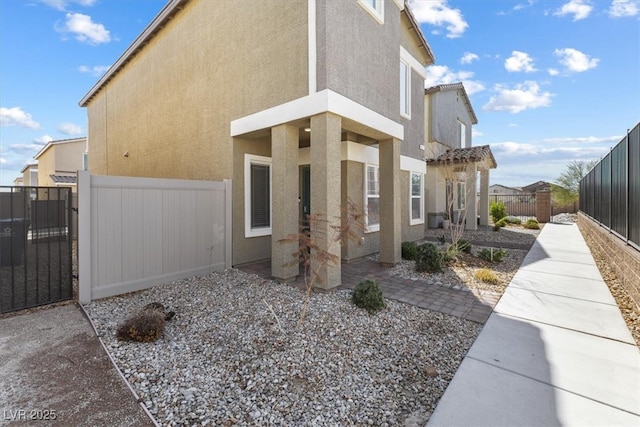 view of side of home featuring a gate, fence, and stucco siding