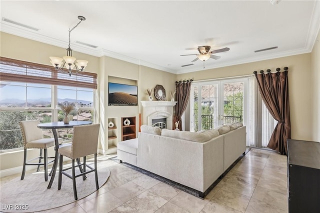 living room with a glass covered fireplace, visible vents, crown molding, and ceiling fan with notable chandelier