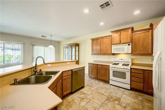 kitchen with pendant lighting, visible vents, brown cabinetry, a sink, and white appliances