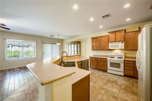 kitchen with white appliances, brown cabinetry, a sink, and visible vents