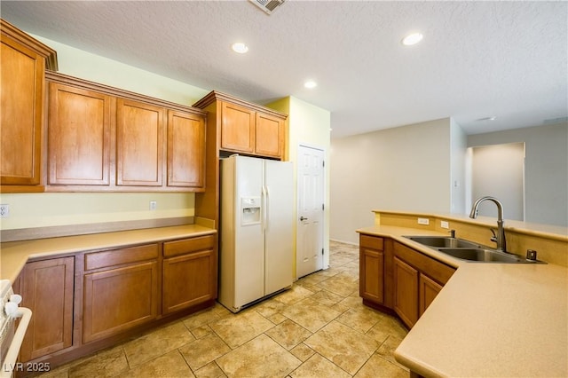 kitchen featuring recessed lighting, white refrigerator with ice dispenser, a sink, light countertops, and brown cabinetry