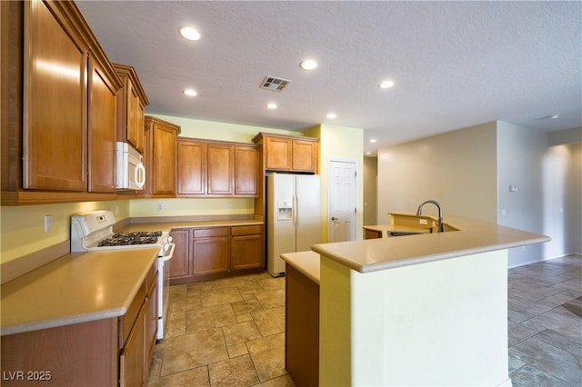 kitchen with a kitchen island with sink, white appliances, a sink, visible vents, and brown cabinets