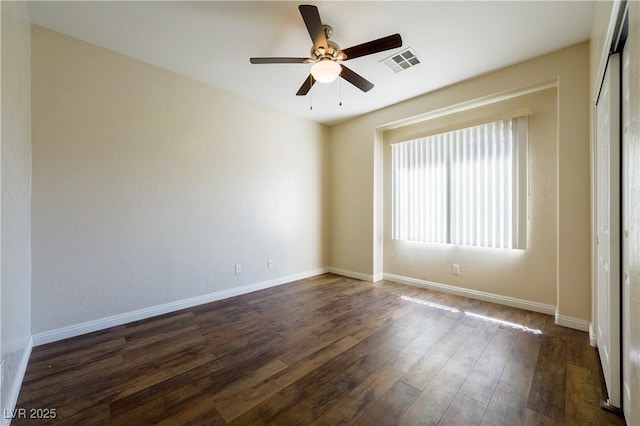 spare room featuring baseboards, visible vents, ceiling fan, and dark wood-style flooring