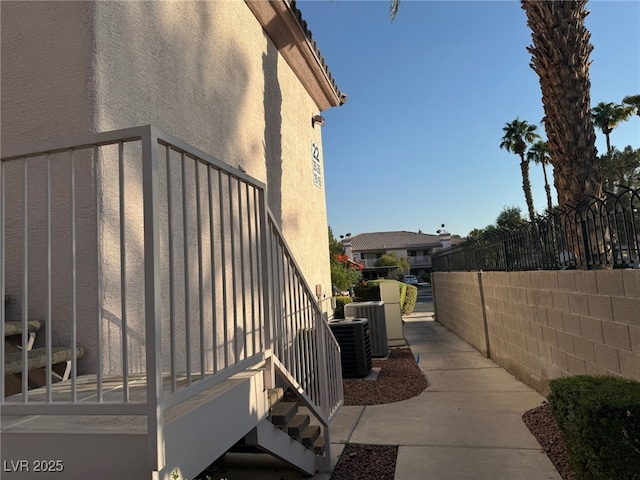 view of side of home featuring cooling unit, fence, and stucco siding