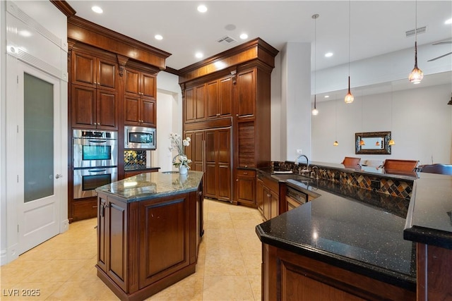 kitchen featuring stainless steel appliances, a peninsula, a sink, hanging light fixtures, and dark stone countertops