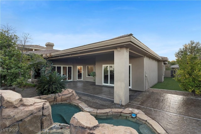 rear view of property with an in ground hot tub, a patio, and stucco siding