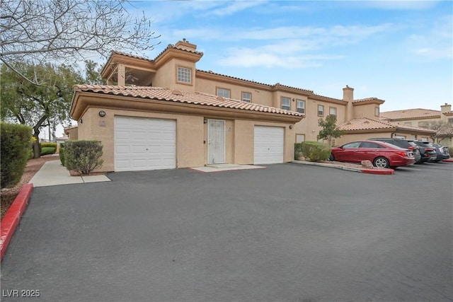 mediterranean / spanish-style home featuring a garage, aphalt driveway, a tile roof, and stucco siding