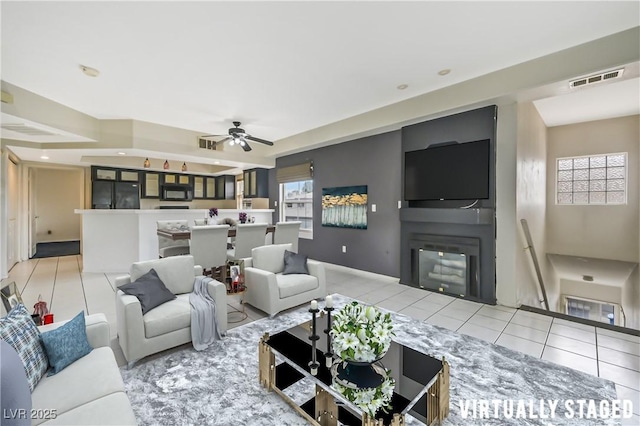 living room featuring a glass covered fireplace, visible vents, tile patterned flooring, and ceiling fan
