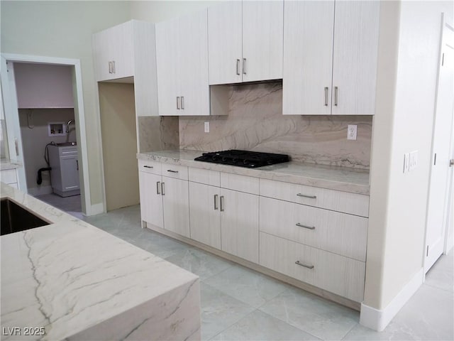 kitchen with black gas cooktop, a sink, baseboards, backsplash, and light stone countertops