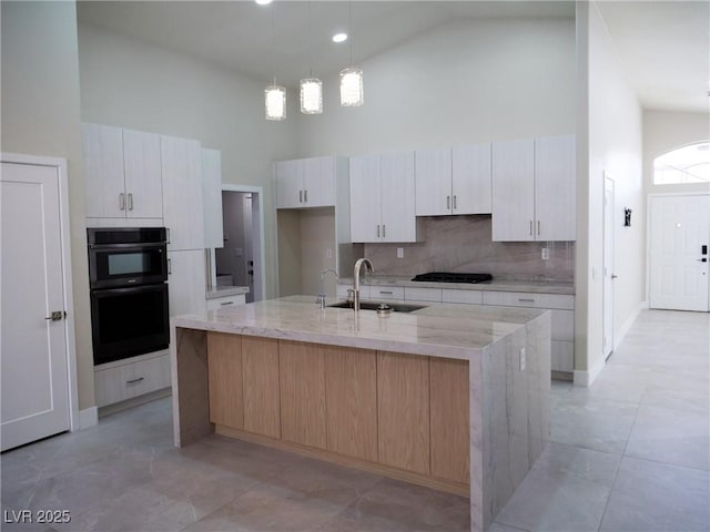 kitchen featuring a spacious island, a sink, light stone countertops, high vaulted ceiling, and black appliances