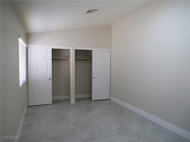 unfurnished bedroom with baseboards, visible vents, vaulted ceiling, and multiple closets