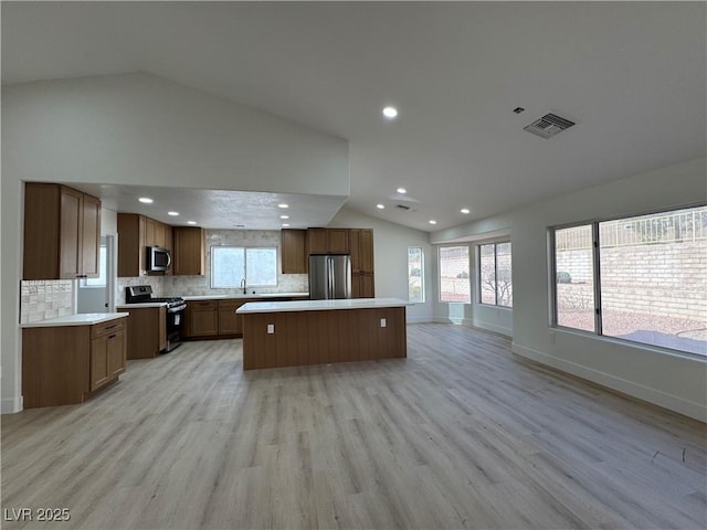 kitchen with light wood finished floors, lofted ceiling, a kitchen island, appliances with stainless steel finishes, and open floor plan