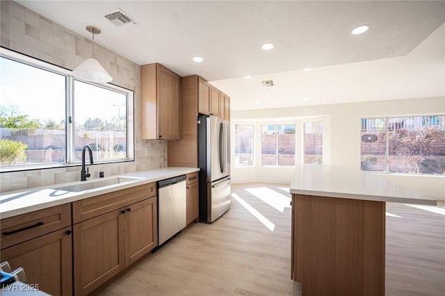 kitchen featuring visible vents, a sink, decorative backsplash, stainless steel appliances, and light wood-type flooring