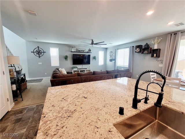 kitchen with visible vents, ceiling fan, a sink, light stone countertops, and baseboards