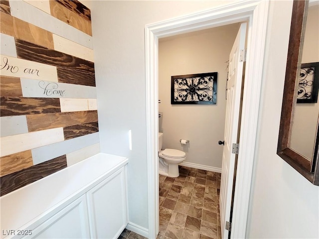 bathroom with stone finish flooring, toilet, and baseboards