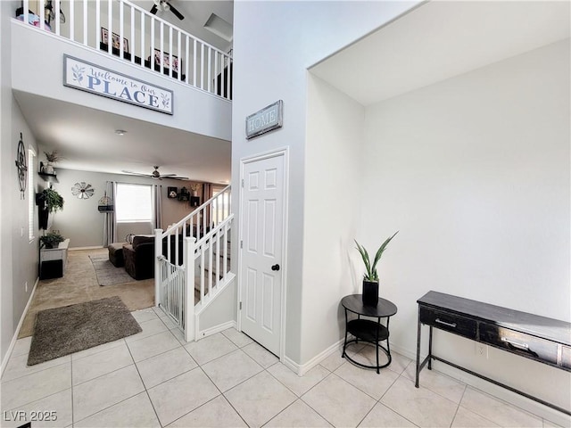 staircase featuring baseboards, a high ceiling, a ceiling fan, and tile patterned floors