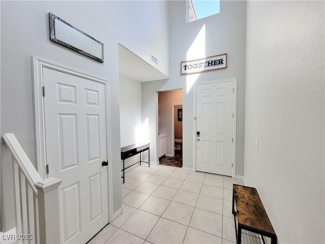 foyer with baseboards, visible vents, a high ceiling, stairs, and light tile patterned flooring