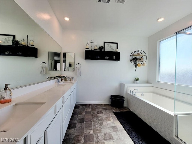 bathroom featuring stone finish floor, a garden tub, a sink, and double vanity