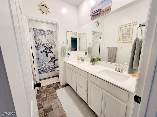 bathroom with stone finish flooring, a sink, toilet, and double vanity