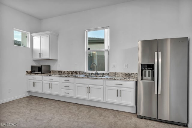 kitchen featuring baseboards, light stone countertops, stainless steel appliances, white cabinetry, and a sink