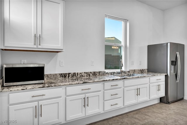 kitchen featuring stainless steel appliances, white cabinets, a sink, and light stone counters