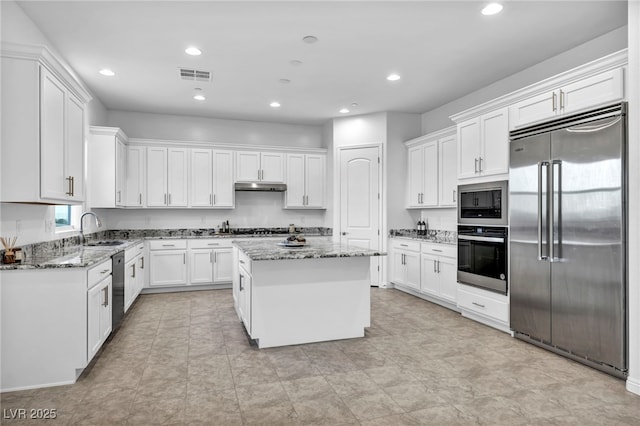 kitchen with visible vents, white cabinets, a kitchen island, built in appliances, and under cabinet range hood