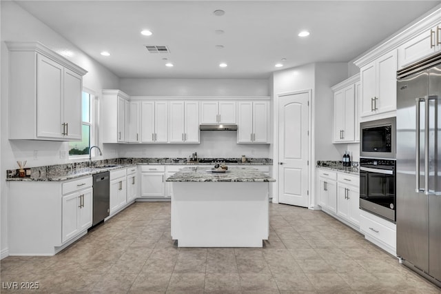 kitchen featuring built in appliances, under cabinet range hood, white cabinetry, visible vents, and light stone countertops