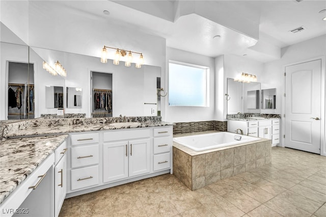 full bathroom with a garden tub, two vanities, a sink, visible vents, and a spacious closet