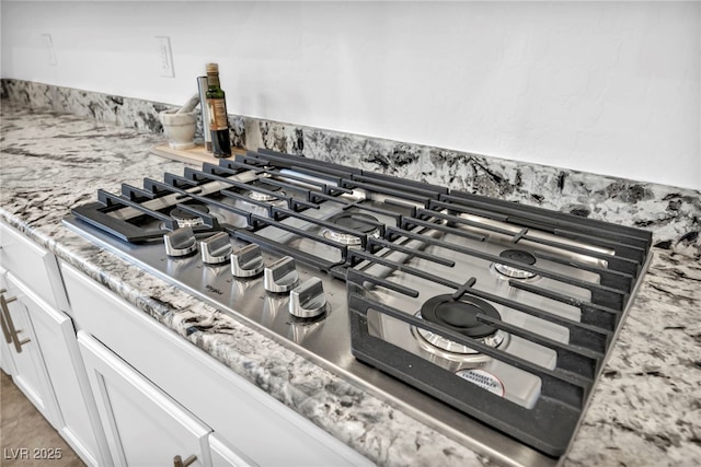 interior details with white cabinetry, stainless steel gas cooktop, and light stone counters